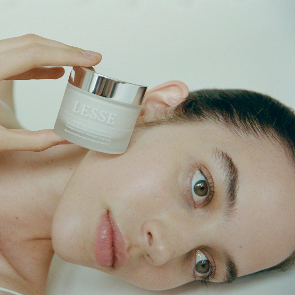 Model with glowing skin holding LESSE Essential Moisturizer – clean, plant-based skincare with Tremella mushroom and natural Vitamin C for radiant hydration - Gllosse