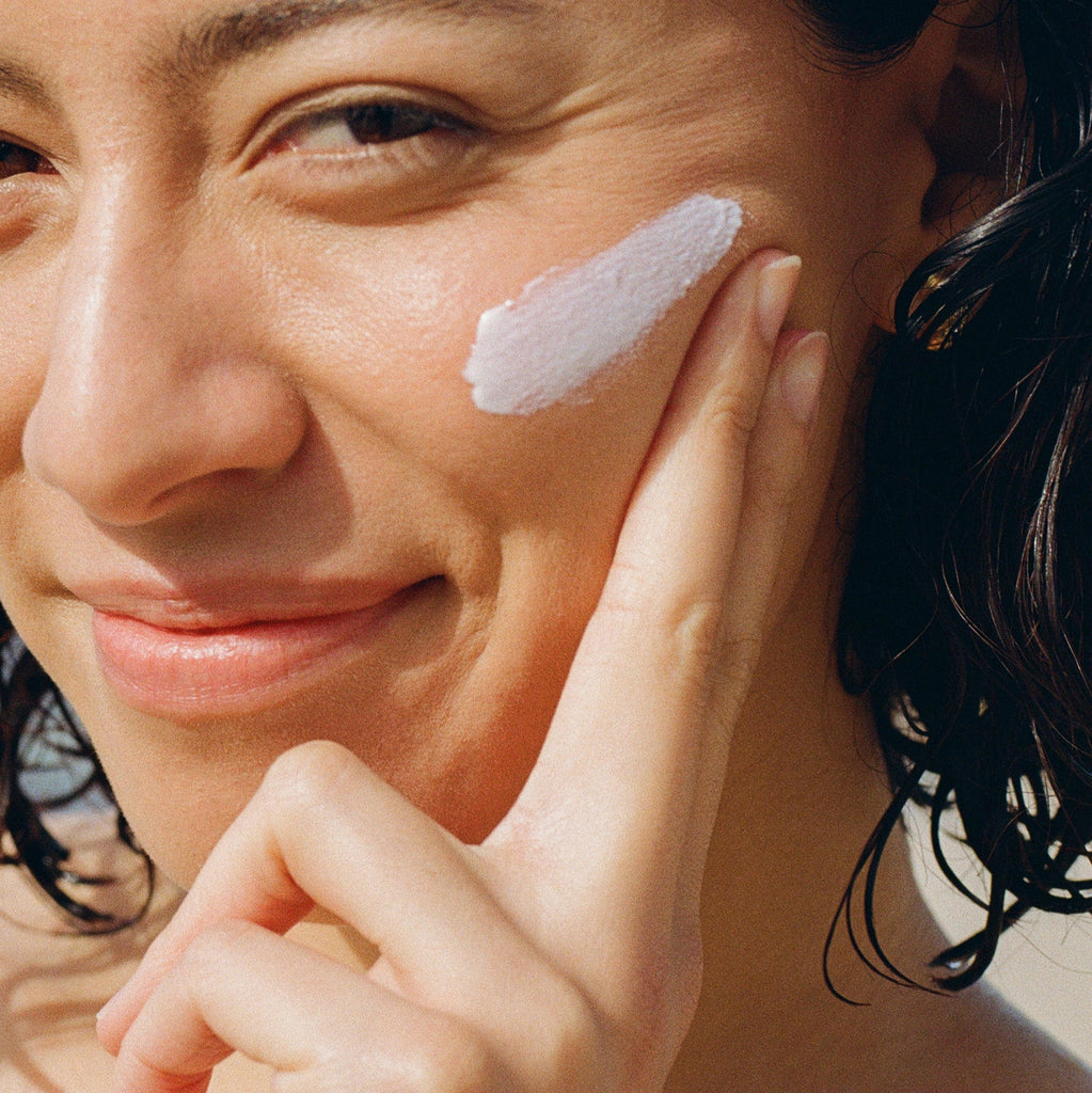 Woman applying a Mother Face & Body SPF cream to her face with a close-up view.