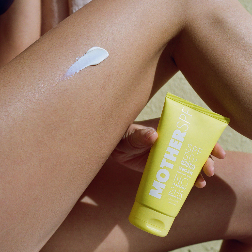 Person applying Mother SPF 50 Face & Body to their leg with a yellow 'Mother Sun' tube.